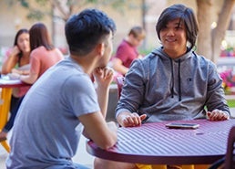 photo of 2 students sitting outside in courtyard talking