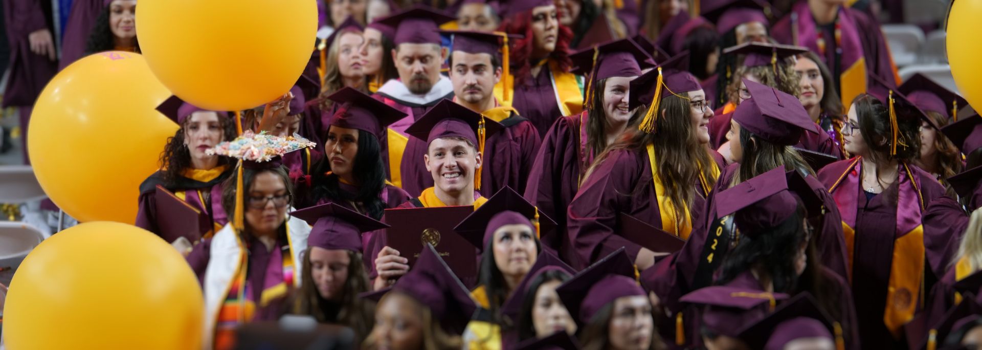 A large crowd of students wearing regalia happily walking together