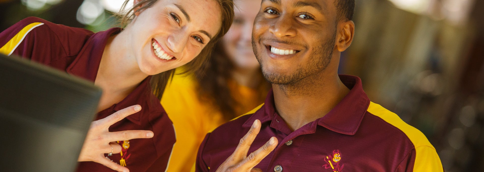 Two students smiling at the camera making pitchforks with their hands