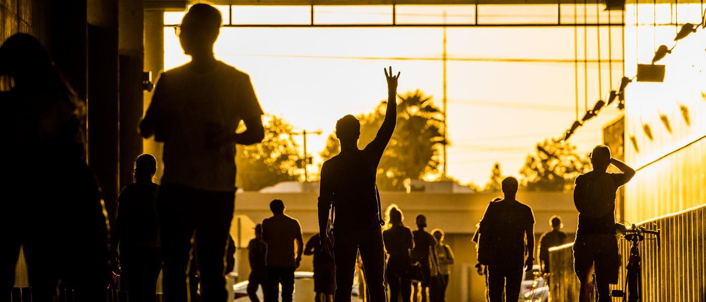 silhouettes of people walking through an outdoor hallway with the sun behind them