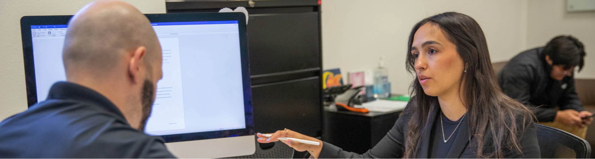 Student and advisor discussing in front of a computer monitor in an office setting.