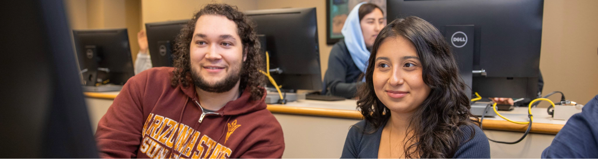 Two people smiling in a computer lab with monitors in the background.