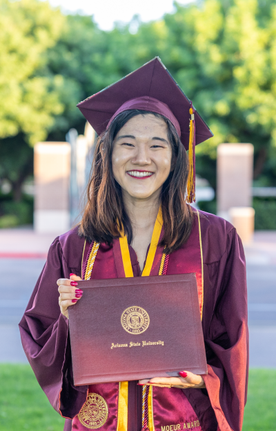 Graduate holding diploma cover outside on campus
