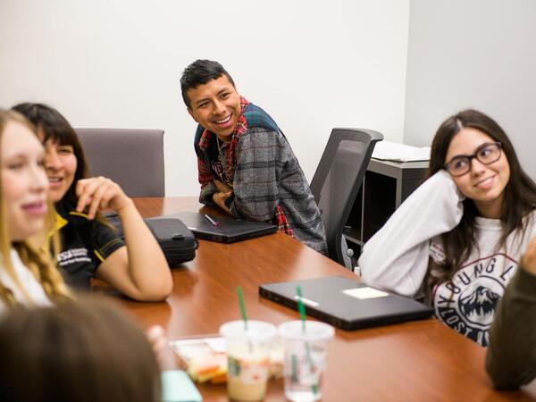 A group of students around a conference table watching something in the distance