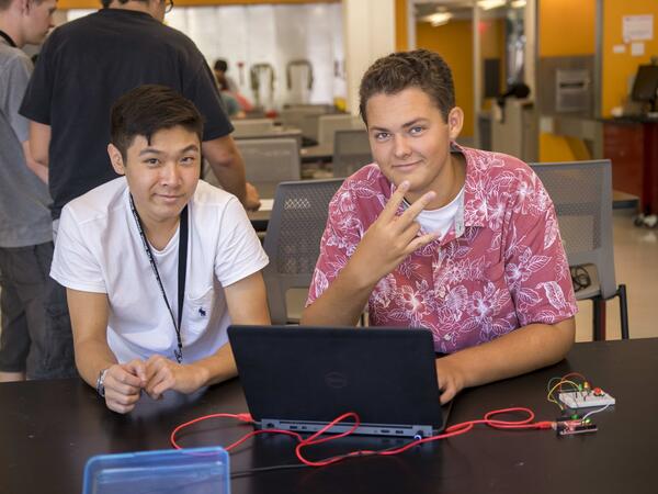 two male students looking at the camera, one is making a pitchfork symbol with his hands