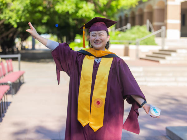 Jun Qian smiling outside while holding up an ASU pitch fork and wearing regalia